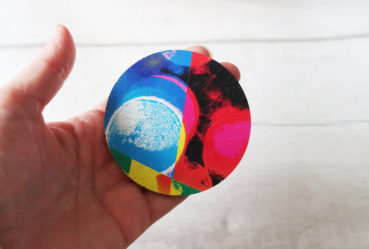 Colorful circular brooch held in a hand against a white background
