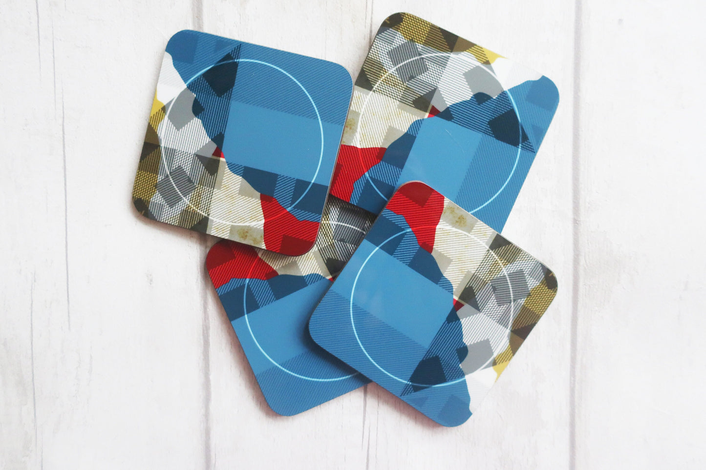 Set of four geometric-patterned coasters on a white wooden surface