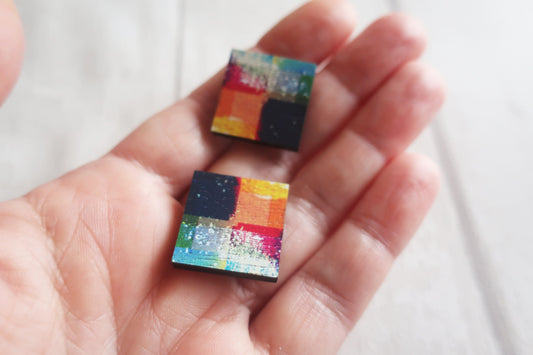 Colorful square earrings held in a hand against a white background