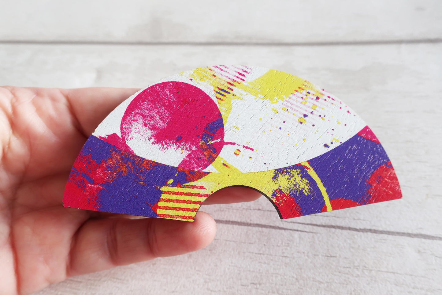 Colorful abstract design on a fan hairclip held by a hand against a light background