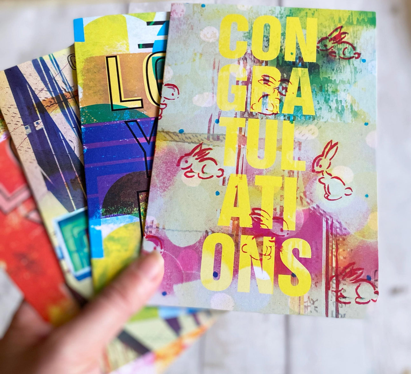 Colorful greeting cards with 'Congratulations' text held by a hand on a light background