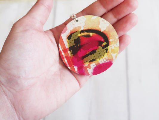 Colorful circular pendant held in a hand against a white background