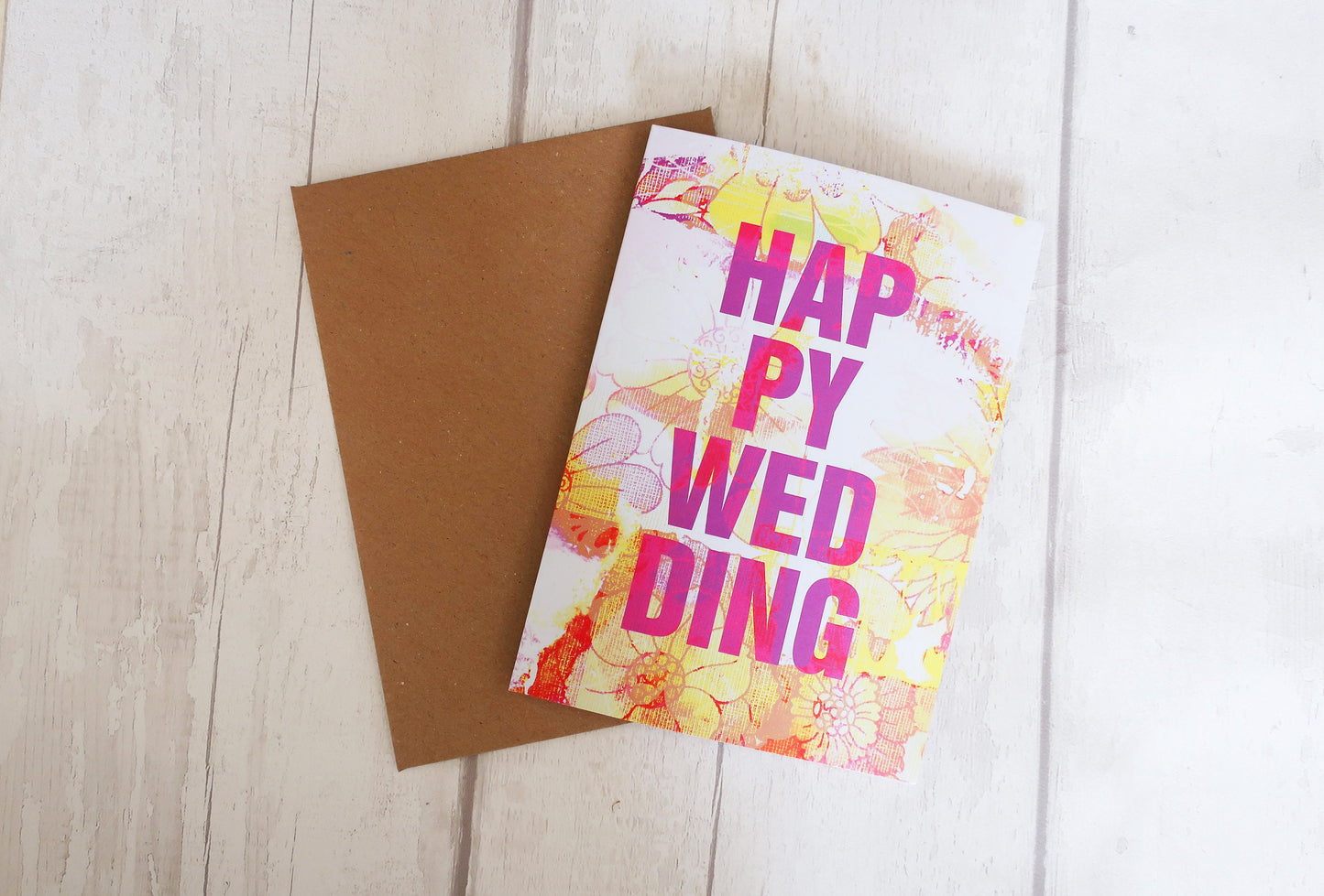 Colorful 'Happy Wedding' card with floral design on a wooden surface