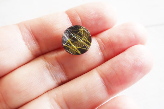 Small round earring held between fingers against a white background