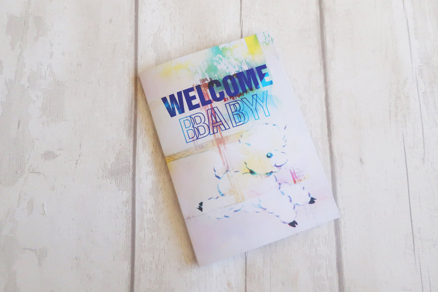 Greeting card with 'Welcome Baby' text on a light wooden surface