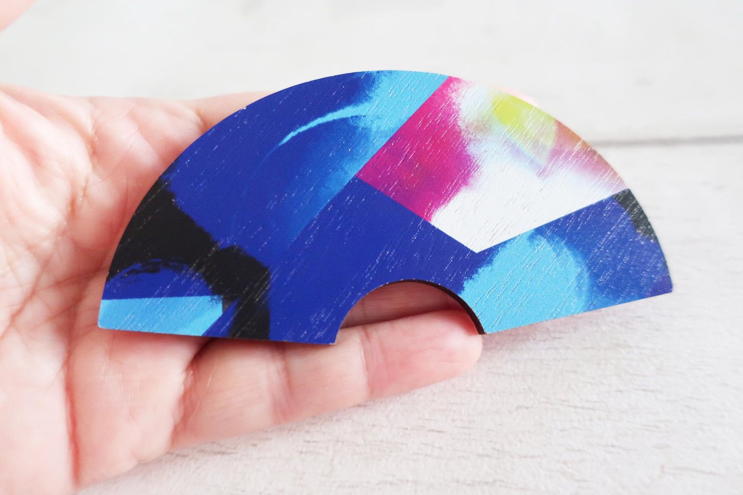 Colorful abstract design on a curved wooden hairclip held in a hand against a white background