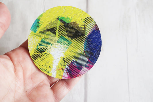 Colorful circular brooch held by a hand against a white background