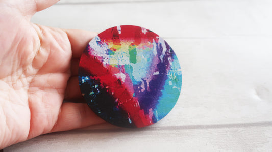 Hand holding a round, multicolored brooch against a light background