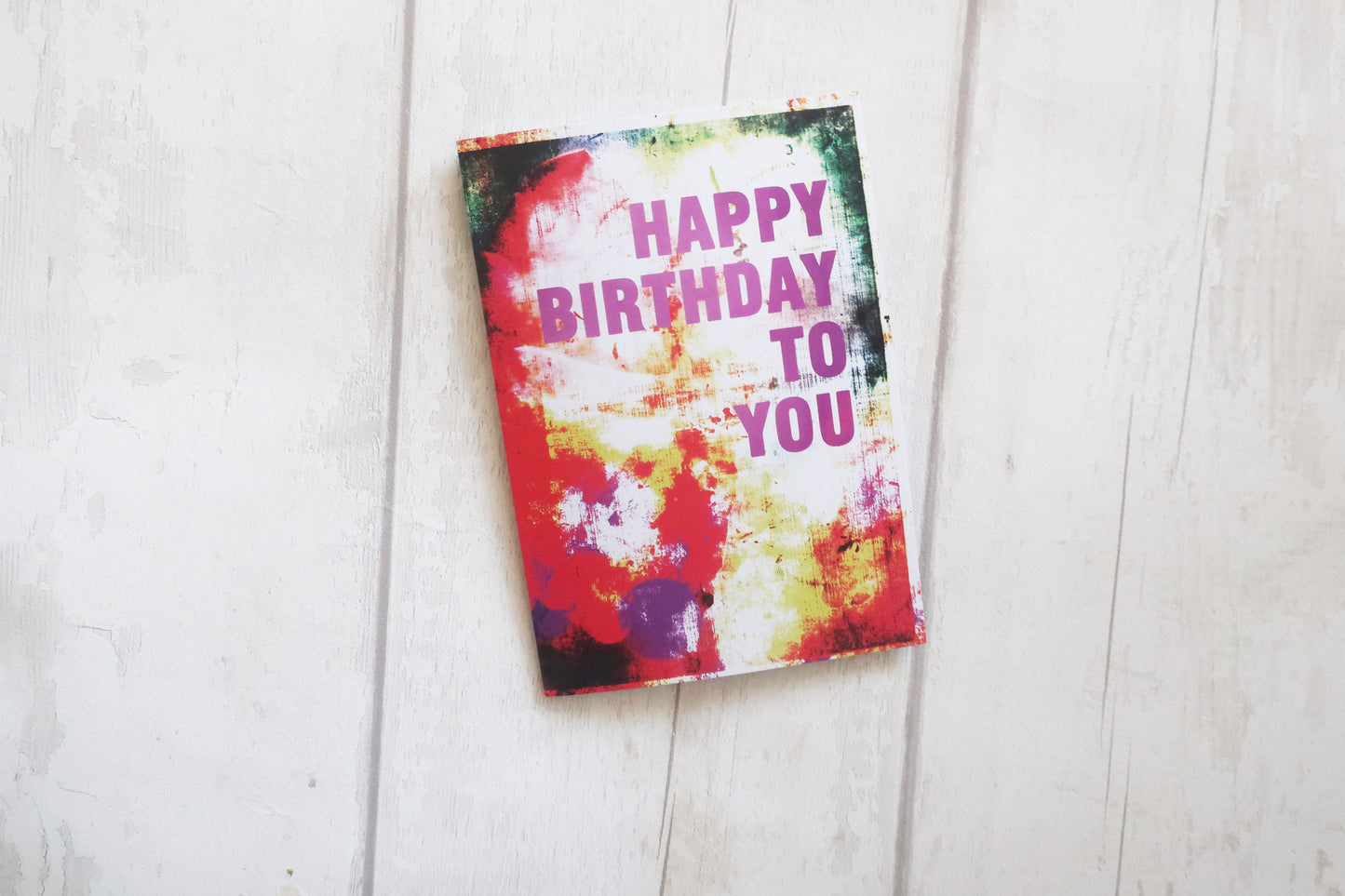 Colorful birthday card with 'Happy Birthday To You' text on a light wooden surface