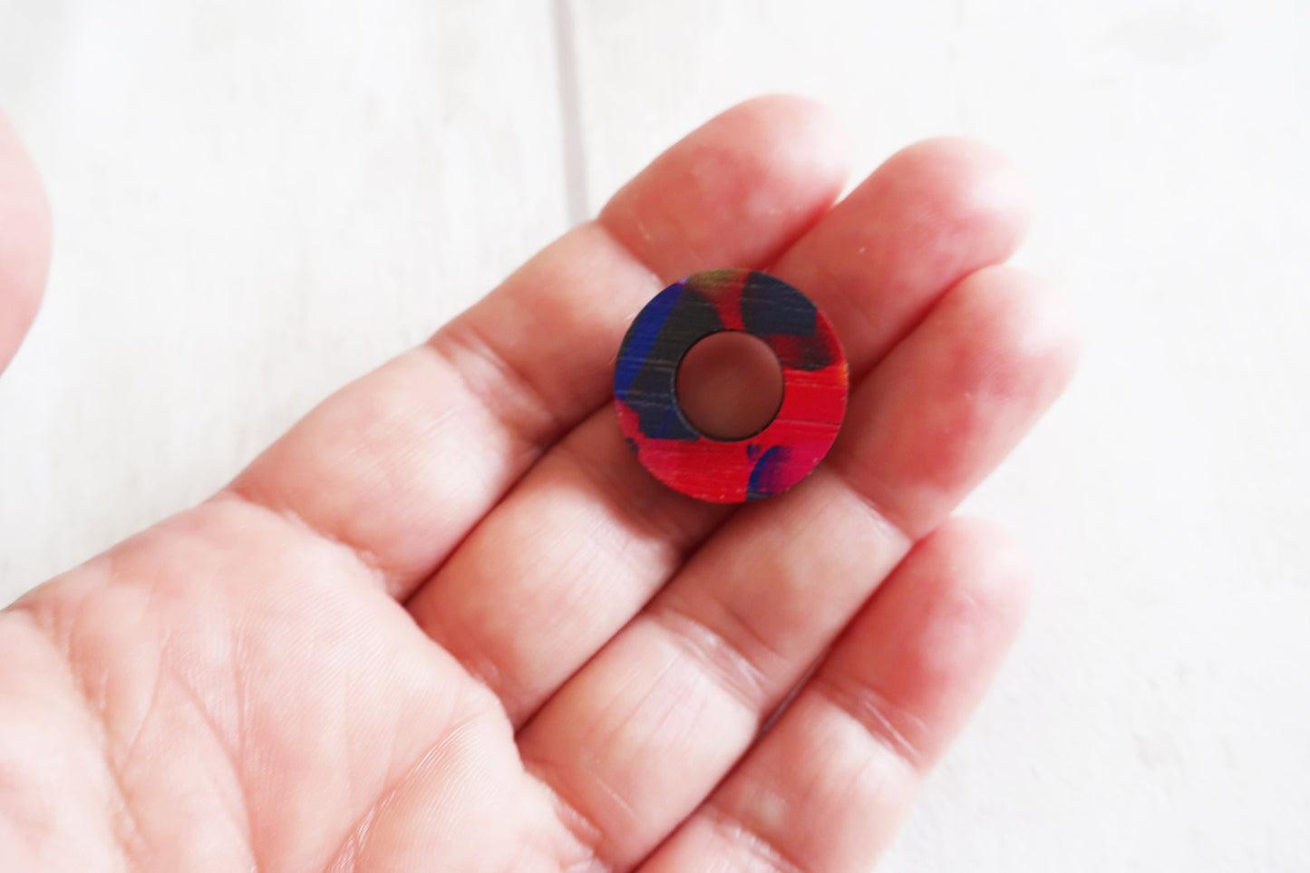 Colorful circular earring held in a hand against a white background