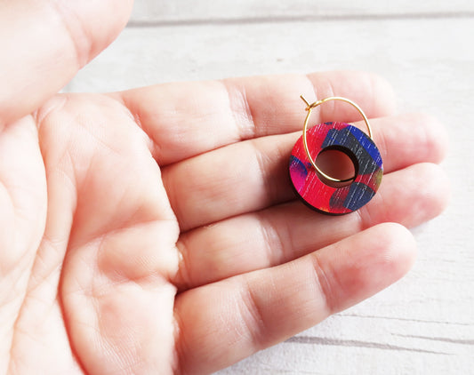 Colorful hoop earring held between fingers on a light background