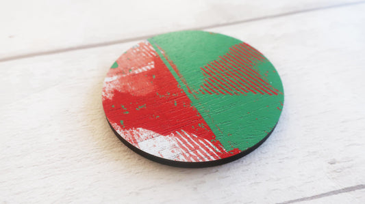 Round brooch with red and green abstract design on a white wooden surface