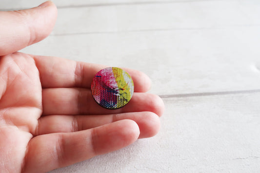 Round colorful pin brooch held in a hand on a light wooden surface