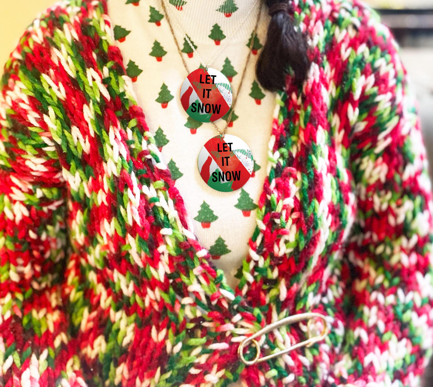 Red, green, and white striped cardigan with 'Let It Snow' necklace on a neutral background