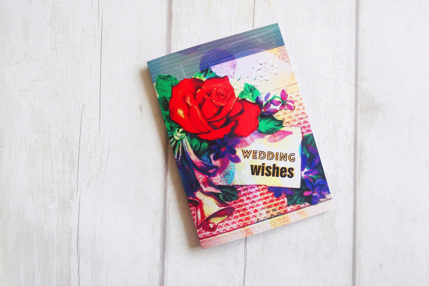 Colorful wedding card with a red rose on a white wooden surface