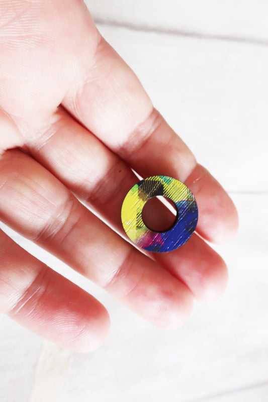 Colorful circular earring held between fingers on a white background