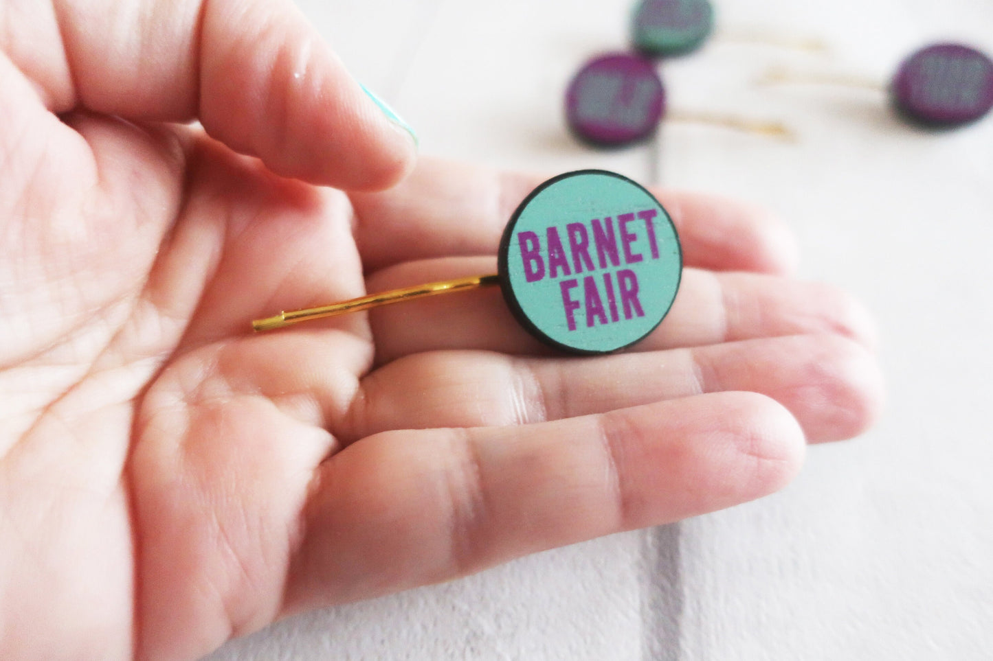 Hand holding a 'Barnet Fair' button badge with a blurred background