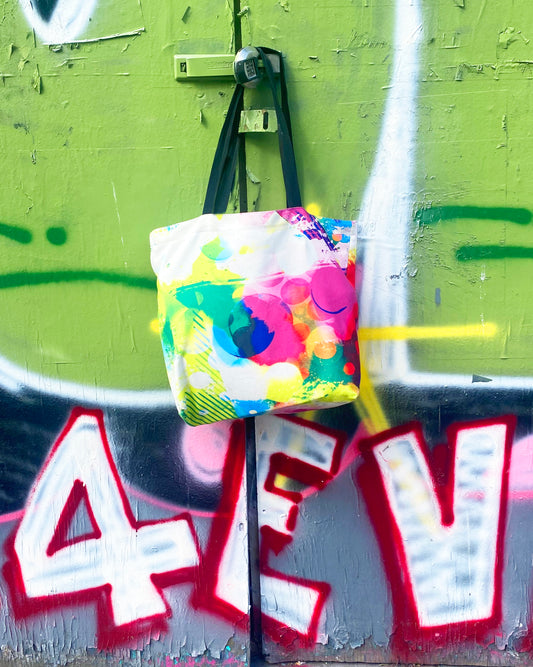 Colorful bag with abstract patterns hanging on a green wall with graffiti.