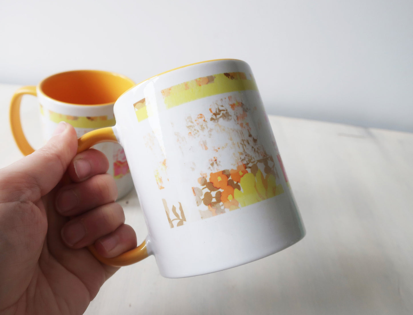 Hand holding a mug with a floral pattern on a plain background