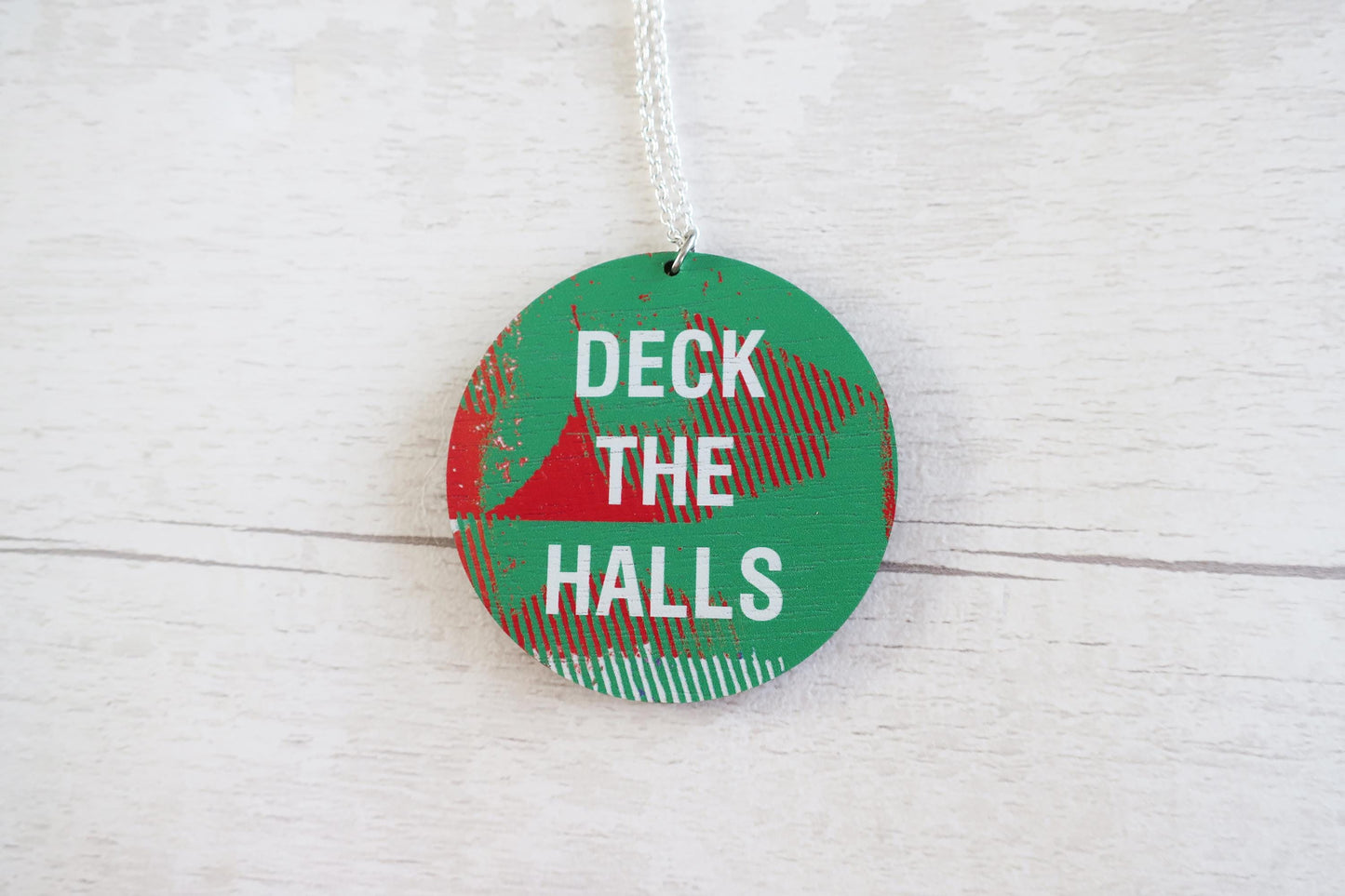 Round Christmas necklace with 'Deck the Halls' text on a white wooden surface