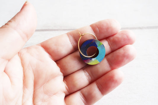 Colorful circular earring held in a hand against a white background