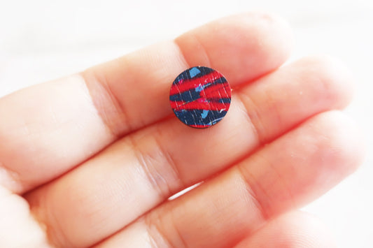 Small round earring with a red and blue pattern held between fingers on a white background