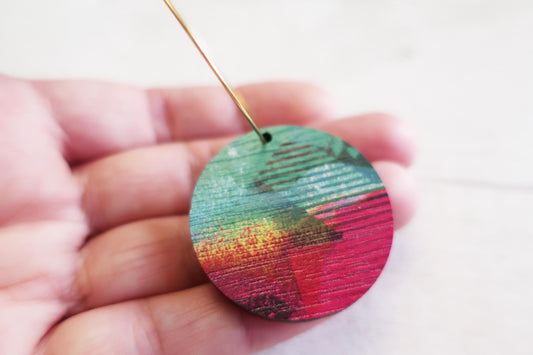 Colorful circular earring held in a hand against a white background