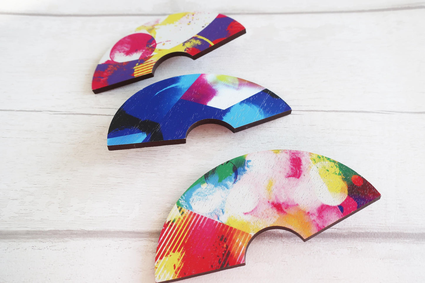 Three colorful, abstract-patterned hairclips on a light wooden surface
