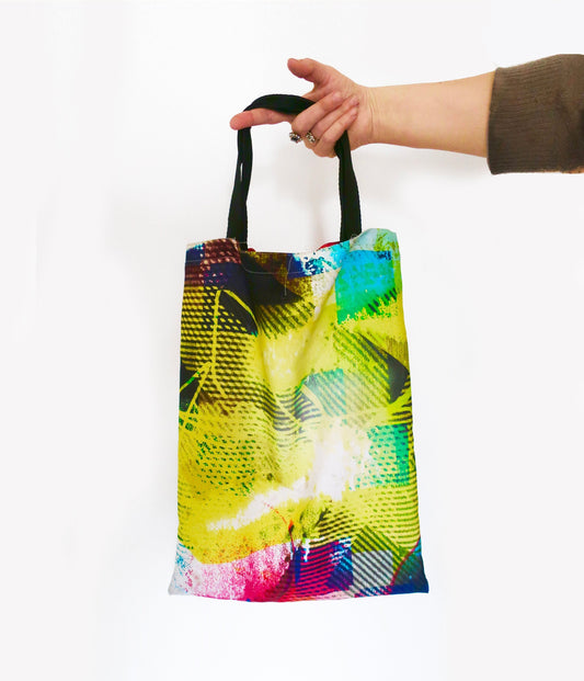 Colorful tote bag with abstract design held by a hand on a white background