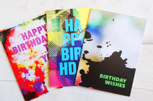 Three colorful birthday cards with different designs on a white surface.