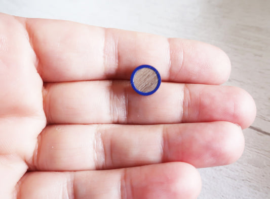 Small blue circular earring held between fingers on a light background