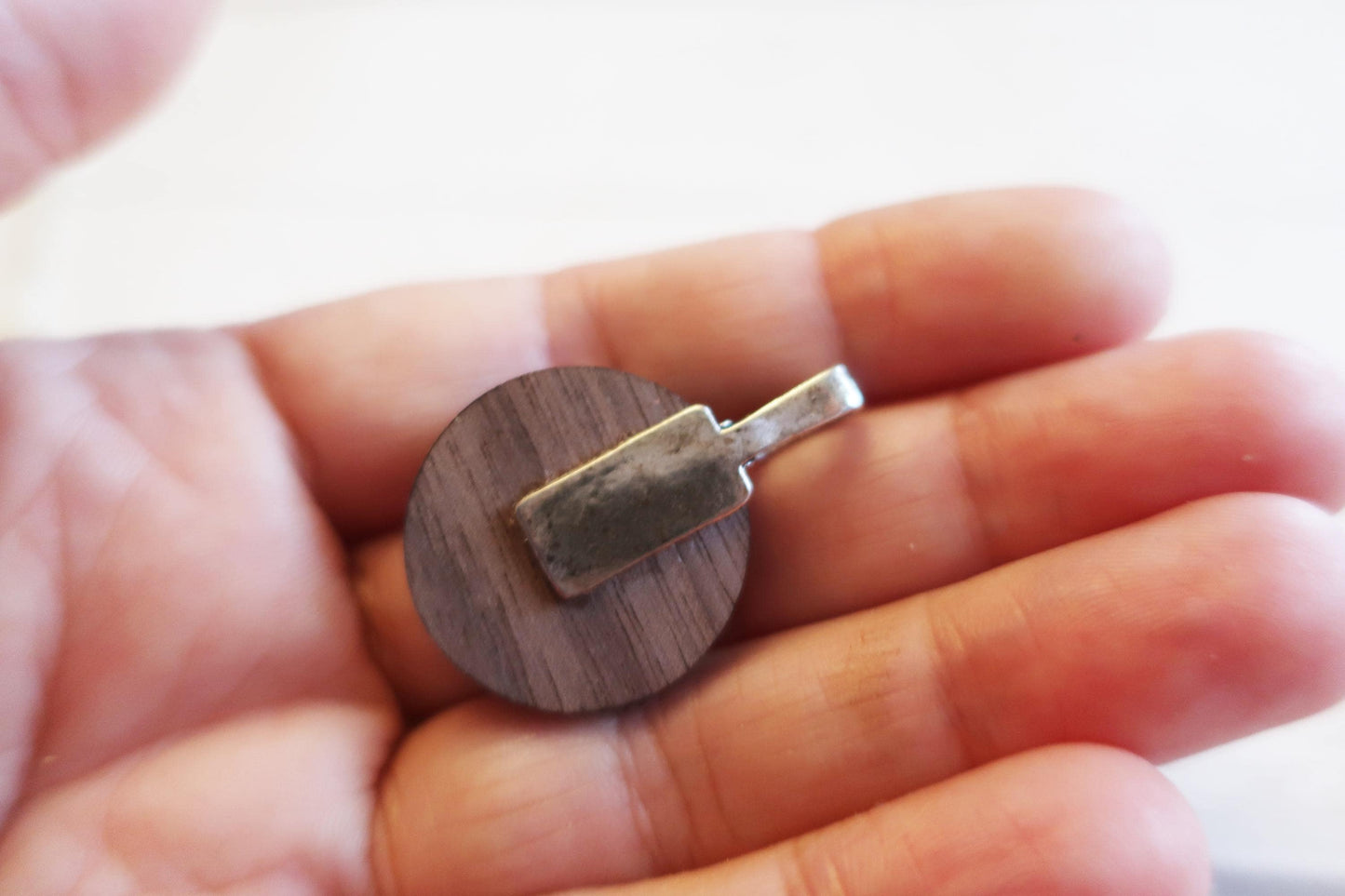 Wooden pendant with metal tag held in a hand against a blurred background