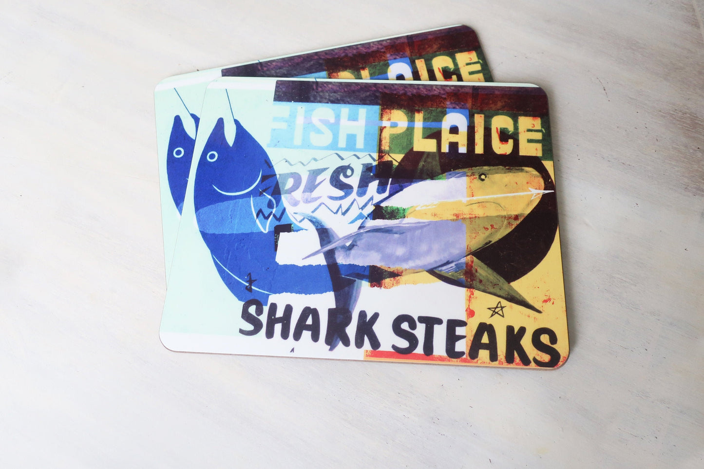 Two fish-themed placemats with colorful designs on a light gray surface.