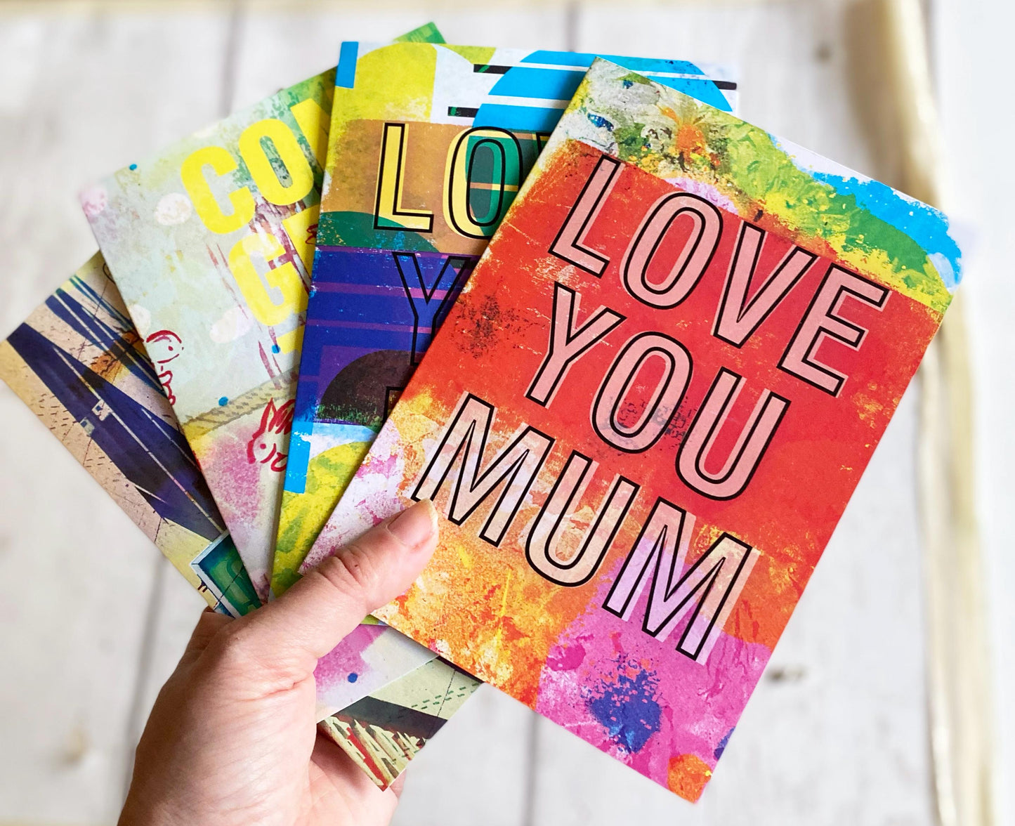 Colorful greeting cards with various messages, including 'LOVE YOU MUM', held by a hand.