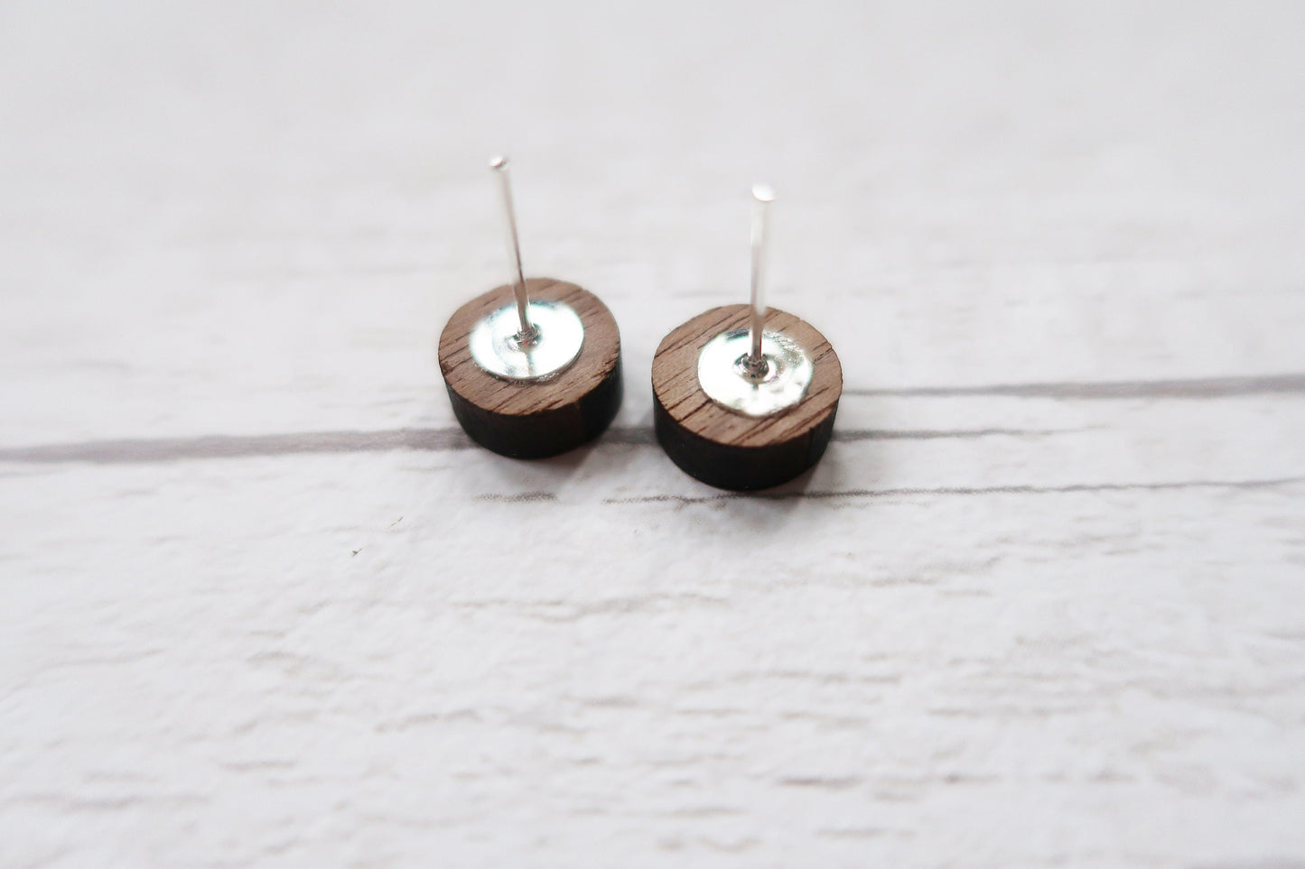 Pair of wooden earrings with silver tops on a light wooden surface