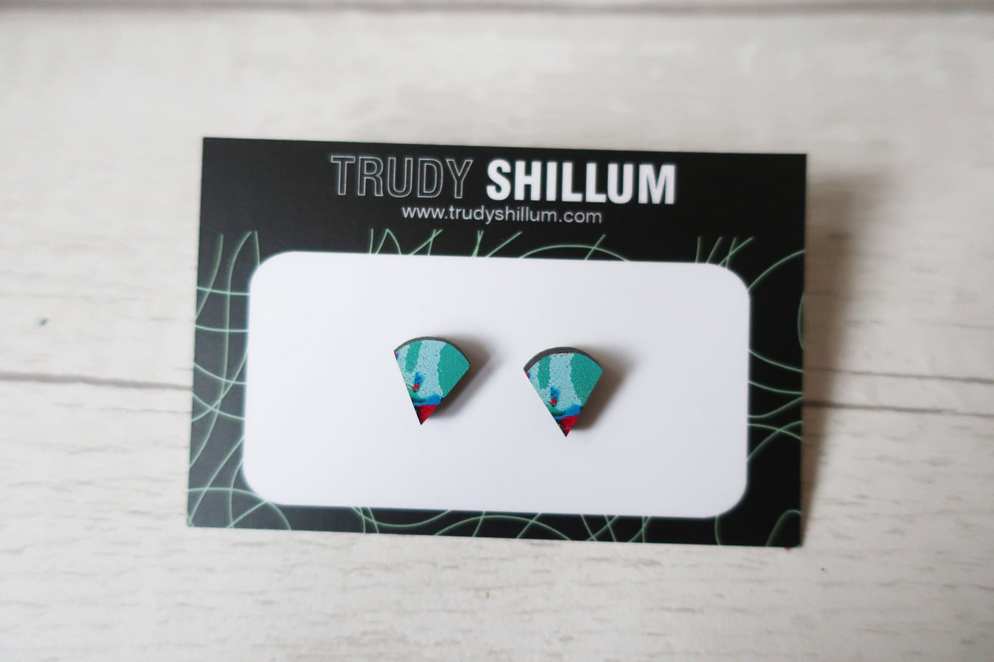 Pair of earrings on a Trudy Shillum branded card with a light wooden background