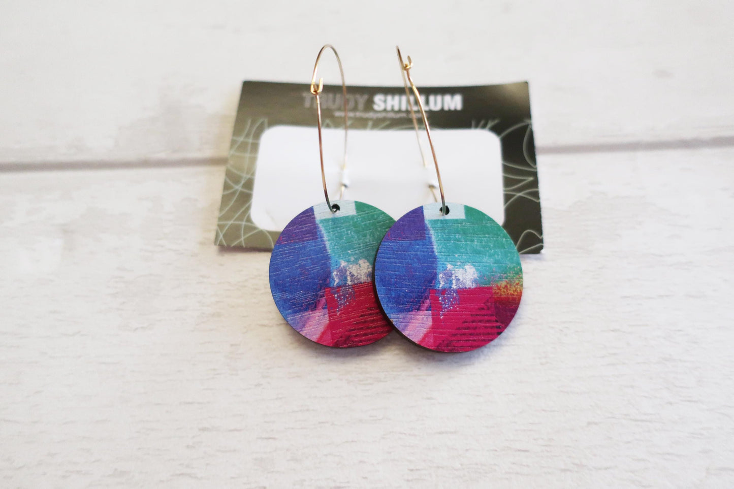 Colorful round earrings on a white surface with a card in the background