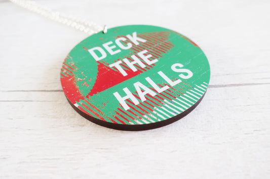 Decorative necklace with 'Deck the Halls' text on a white wooden surface