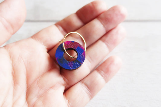 Hand holding a colorful circular earring with gold hoop against a light background