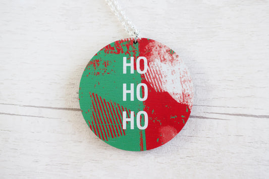 Round Christmas  necklace  with red and green design and 'HO HO HO' text on a white wooden surface.