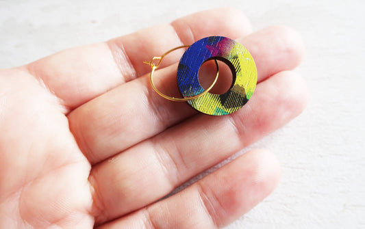 Colorful circular earrings held in a hand against a white background