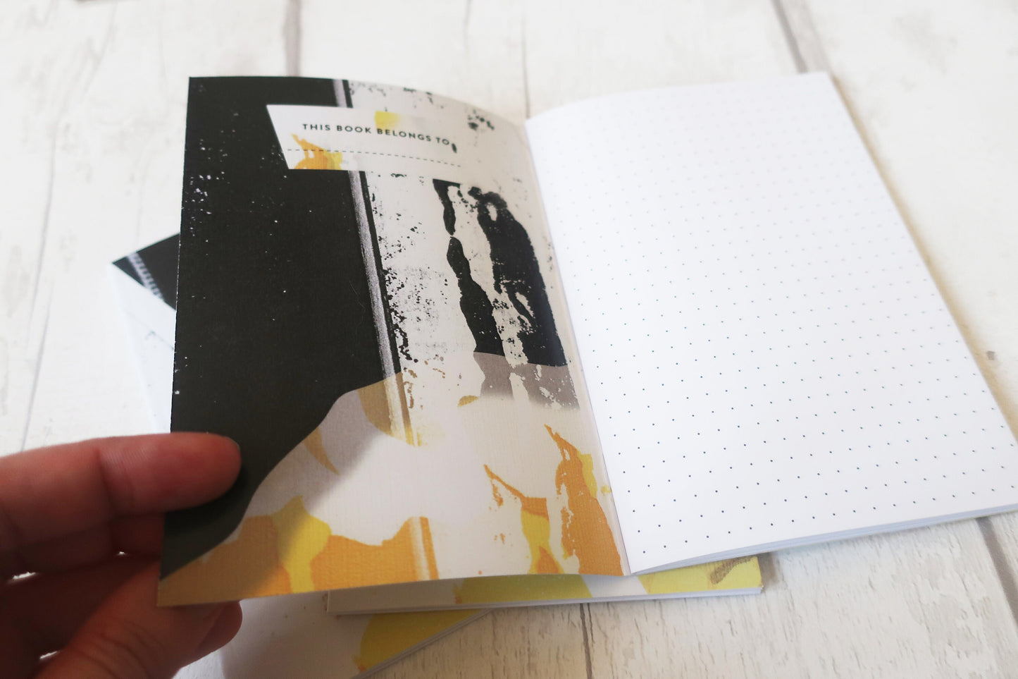 Open notebook with a black cover held by a hand on a light wooden surface