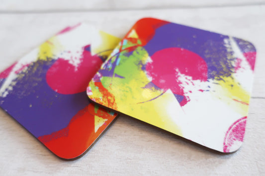 Two colorful abstract coasters on a light wooden surface