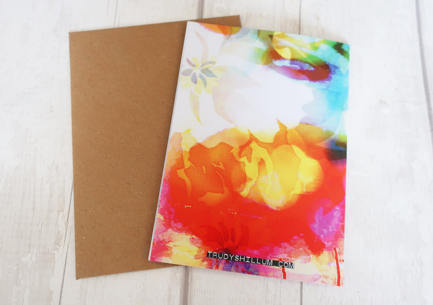 Colorful floral card with a brown envelope on a light wooden surface