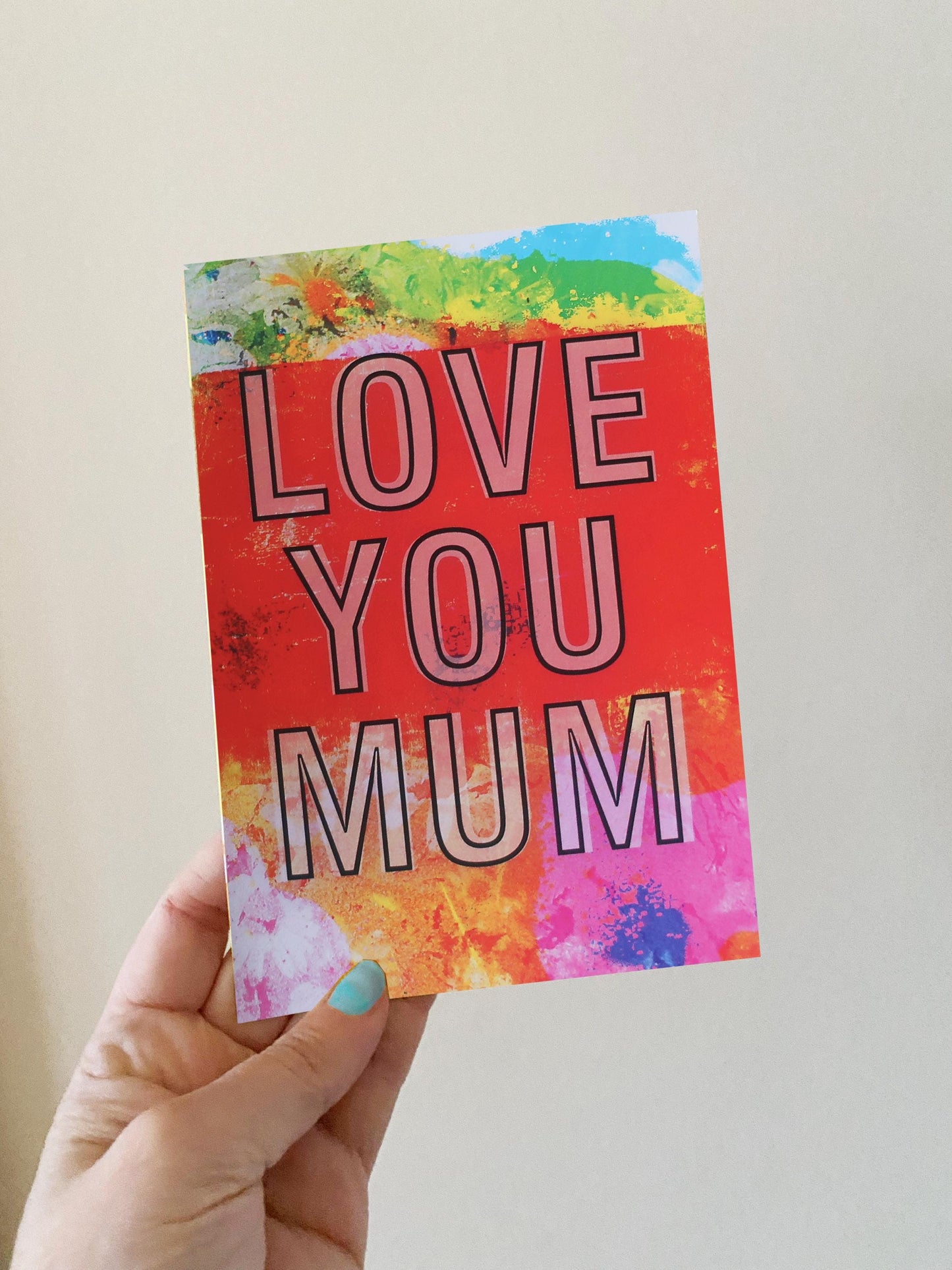 Card with 'LOVE YOU MUM' text held by a hand against a plain background