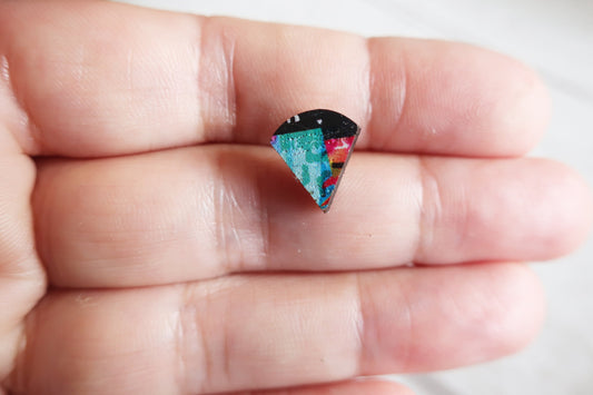 Colorful triangular earring held between fingers against a neutral background