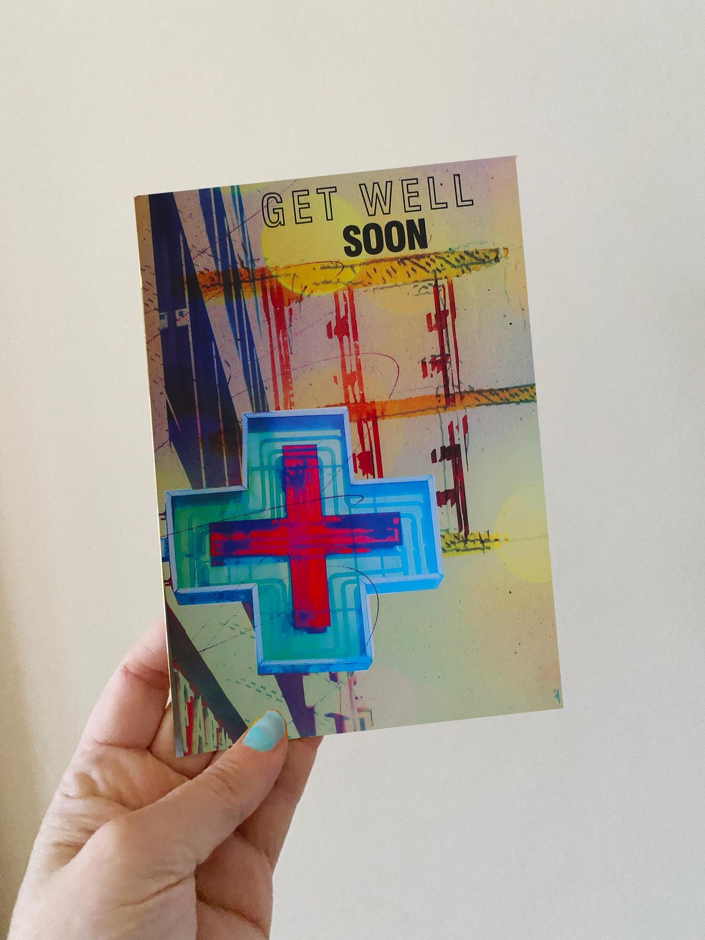 Hand holding a 'Get Well Soon' card with colorful design on a plain background