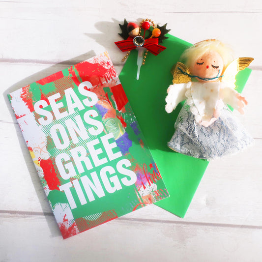 Christmas card with 'Season's Greetings' text, decorative bow, and angel figurine on a white background.