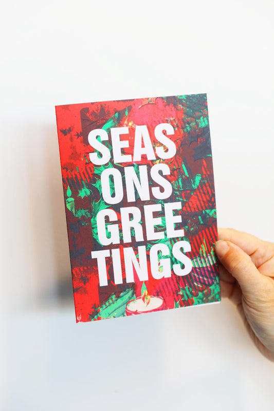 Hand holding a colorful greeting card with 'SEASONS GREETINGS' text on a white background
