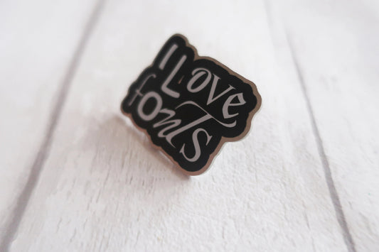 Enamel pin with 'I Love Fonts' text on a white fabric background